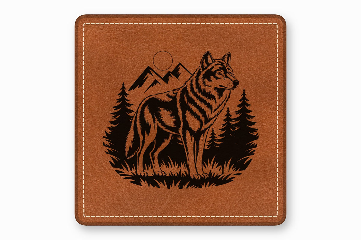 Square brown leather patch with a black engraved design of a wolf standing before mountains and pine trees.