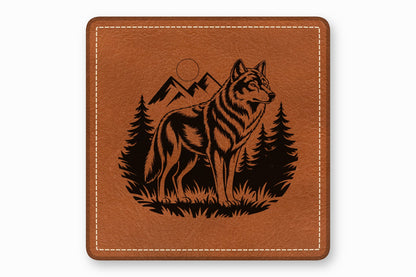 Square brown leather patch with a black engraved design of a wolf standing before mountains and pine trees.