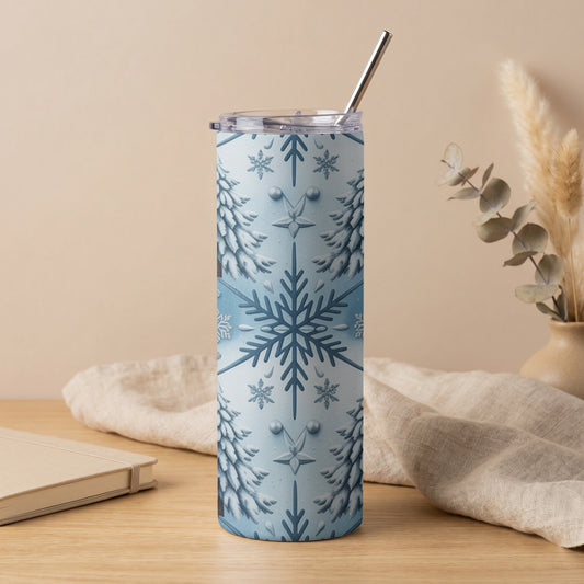 Blue and white snowflake and pine tree patterned tumbler with metal straw on wooden surface.