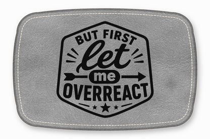 Gray faux leather patch with white stitched borders and a black emblem reading But first let me overreact.