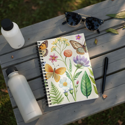 Notebook with watercolor butterflies, flowers, and leaves on a wooden table.
