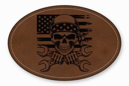 Brown oval leather patch featuring a skull with a bandana, crossed wrenches, and an American flag.