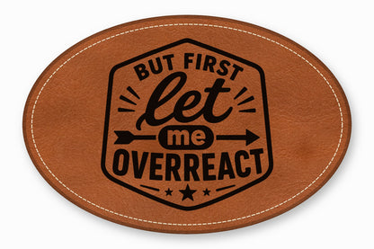 Brown oval leather patch with white stitched border and black text reading But First Let Me Overreact.