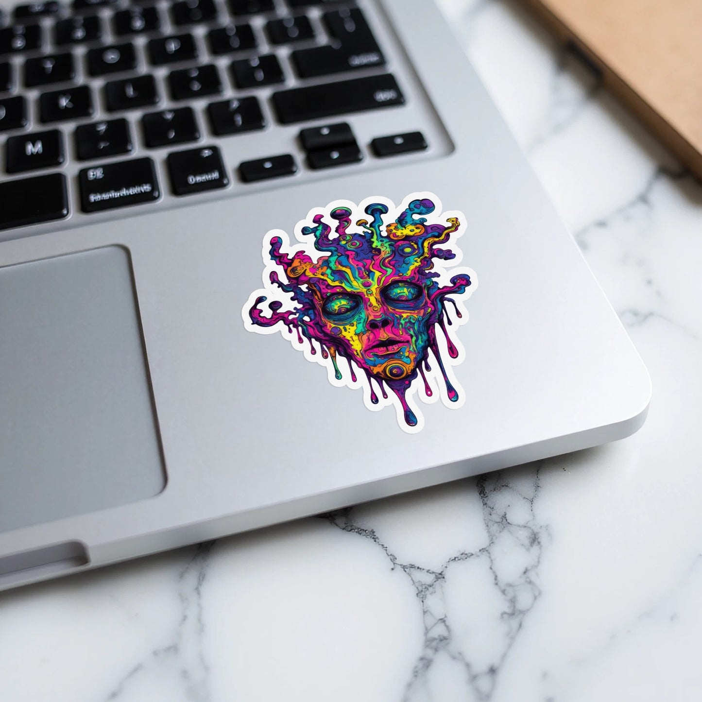 Psychedelic abstract face sticker with melting drips on a laptop keyboard.