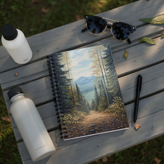 Spiral notebook with forest path painting, two water bottles, and sunglasses on a bench.