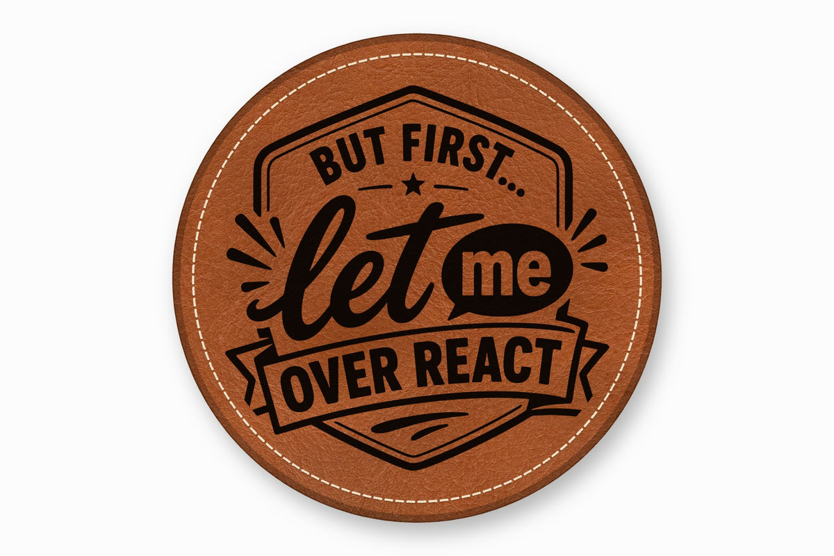 Round brown leather coaster with white stitched edge, featuring the black text But first let me overreact.