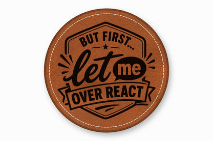 Round brown leather coaster with white stitched edge, featuring the black text But first let me overreact.