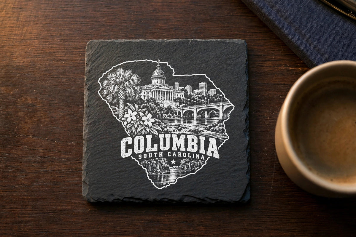 Square black slate coaster engraved with a white design of Columbia, South Carolina landmarks on a wooden table.