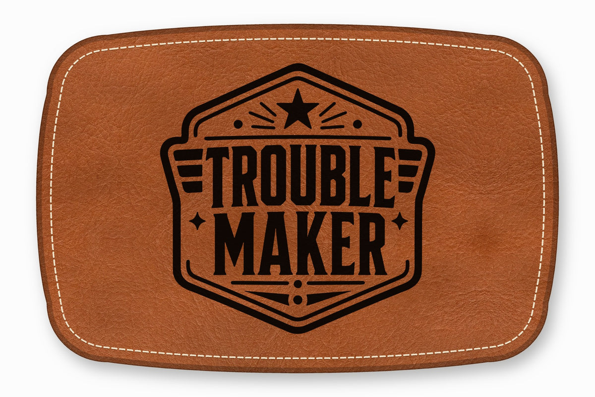 Brown rectangular leather patch with rounded corners, white topstitching, and a black embossed Trouble Maker logo.