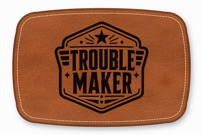 Brown rectangular leather patch with rounded corners, white topstitching, and a black embossed Trouble Maker logo.