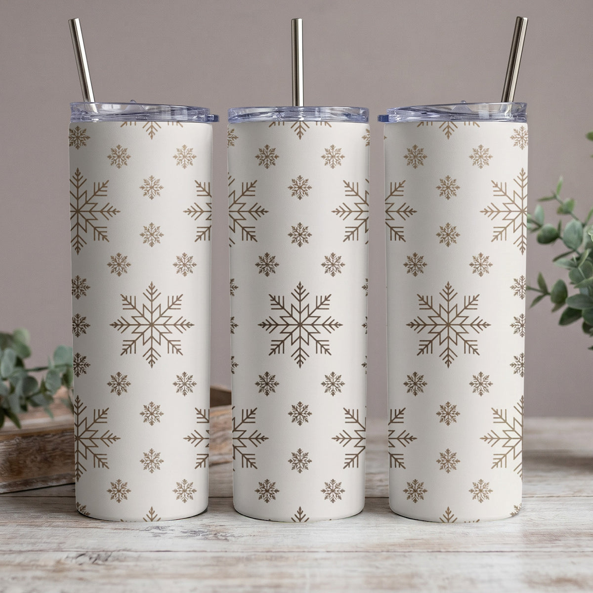 Three white tumblers with a gold snowflake pattern and silver straws.
