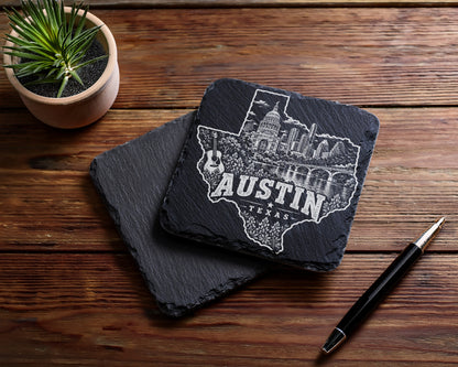 Two square slate coasters rest on a wooden table, featuring an engraved Austin Texas skyline silhouette.