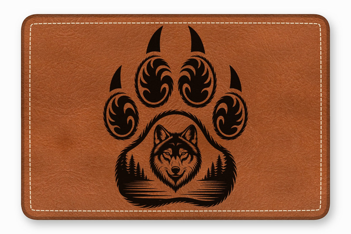 A rectangular brown leather patch features a laser-engraved design of a bear paw containing a wolf and forest.