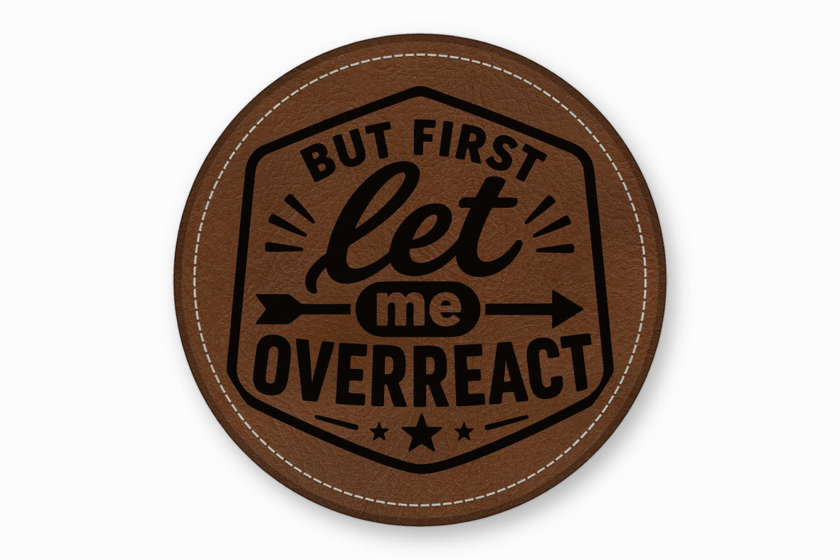 A round brown leather patch with white stitching and the text But First Let Me Overreact.