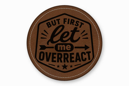 A round brown leather patch with white stitching and the text But First Let Me Overreact.