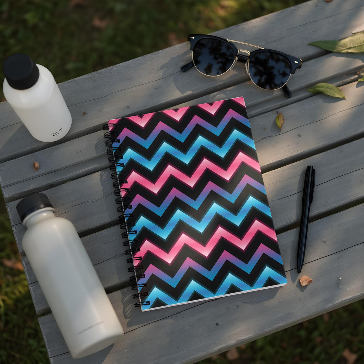 Spiral notebook with pink, blue, and black chevron pattern on a wooden bench.