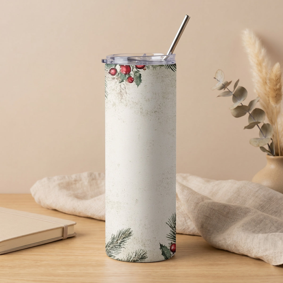 White tumbler with festive holly and pine branch pattern and metal straw.