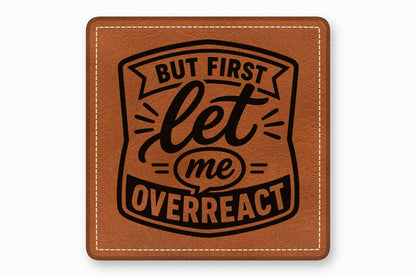 A square brown leather patch with white stitched borders and black text that reads, "BUT FIRST let me OVERREACT".