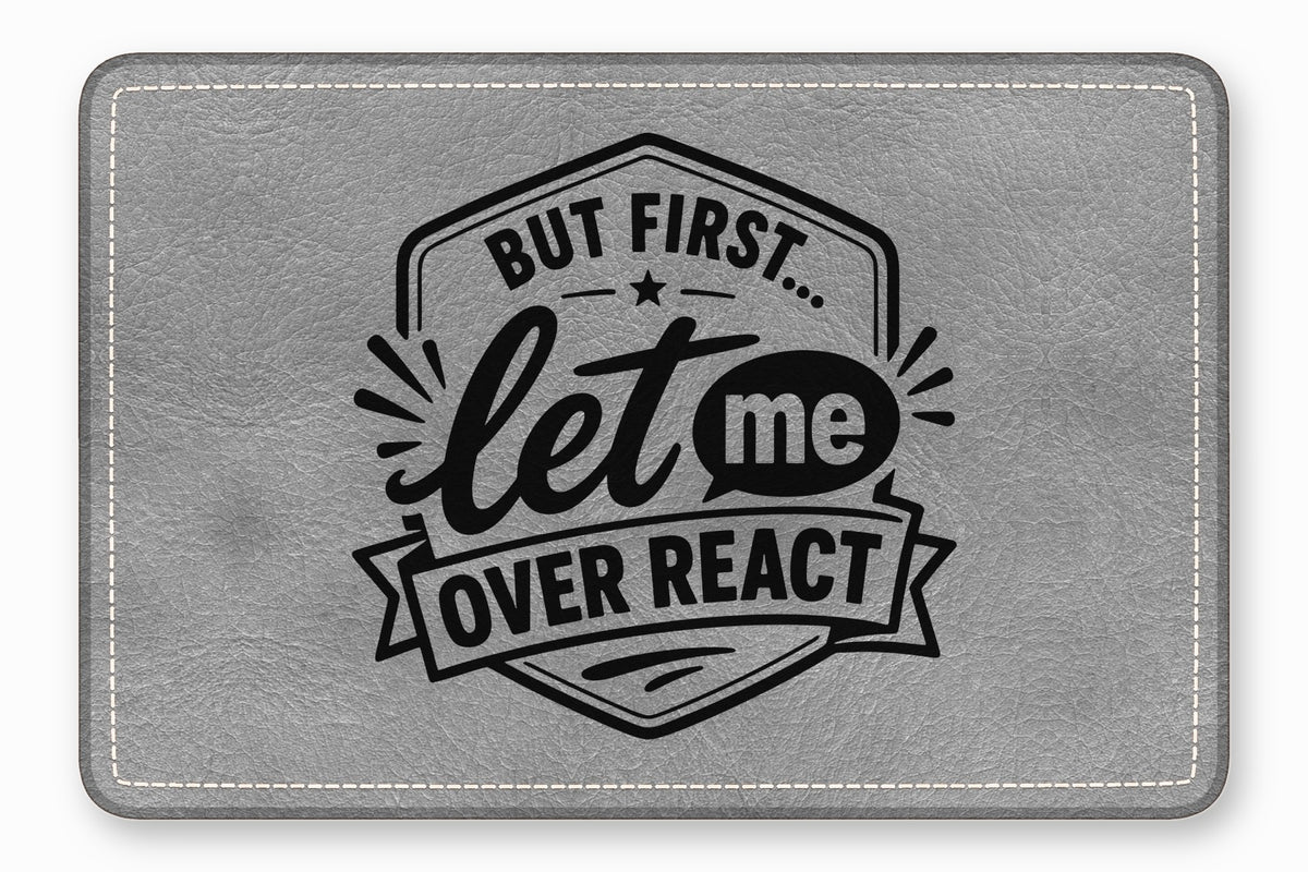 Gray leatherette patch with rounded corners, white stitching, and black engraved text reading But first let me overreact.
