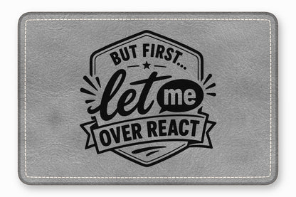 Gray leatherette patch with rounded corners, white stitching, and black engraved text reading But first let me overreact.