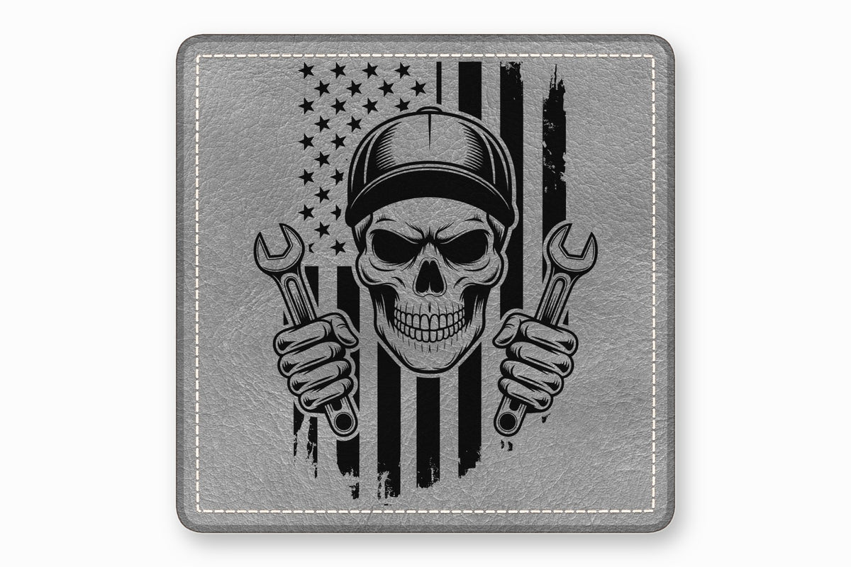Square gray leatherette patch with stitched border, featuring a skull mechanic wearing a cap and holding wrenches against a distressed American flag.