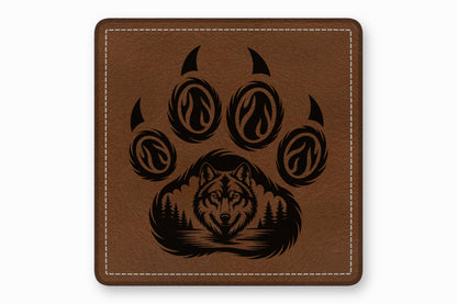 Brown square leather patch engraved with a bear paw containing a wolf face and forest landscape.