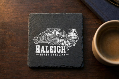 Square black slate coaster engraved with a map outline containing Raleigh landmarks and text.