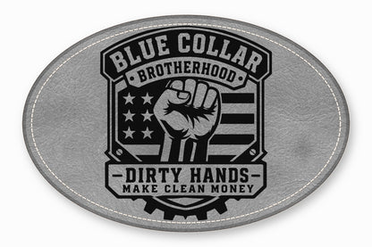 An oval gray leather patch featuring a black graphic with a raised fist, American flag, and text reading Blue Collar Brotherhood and Dirty Hands Make Clean Money.