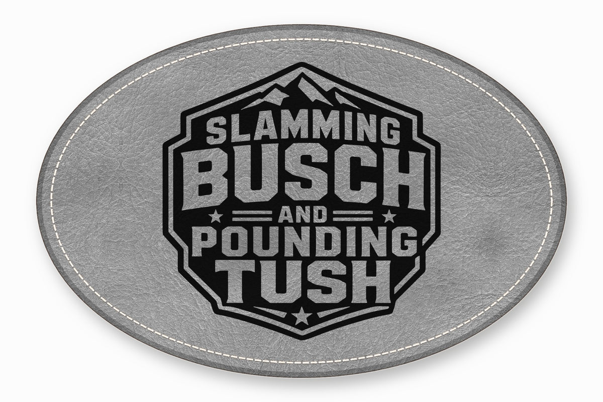 An oval grey leather patch with white stitching featuring a black emblem with the text Slamming Busch and Pounding Tush.