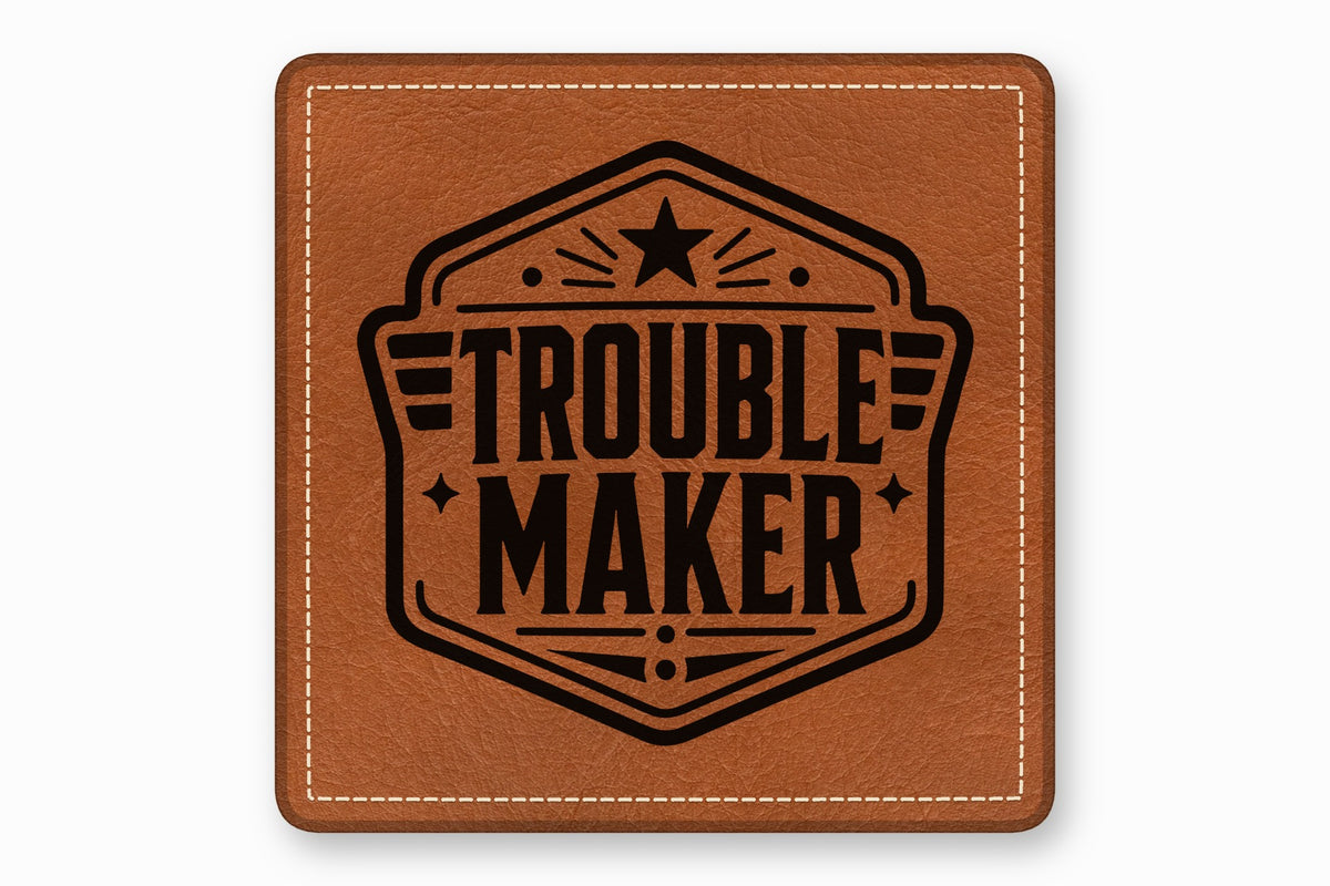 Square brown leather patch with white stitched border and a black emblem reading TROUBLE MAKER.