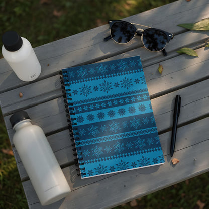 Spiral notebook with blue snowflake pattern on wooden bench with water bottles and sunglasses.
