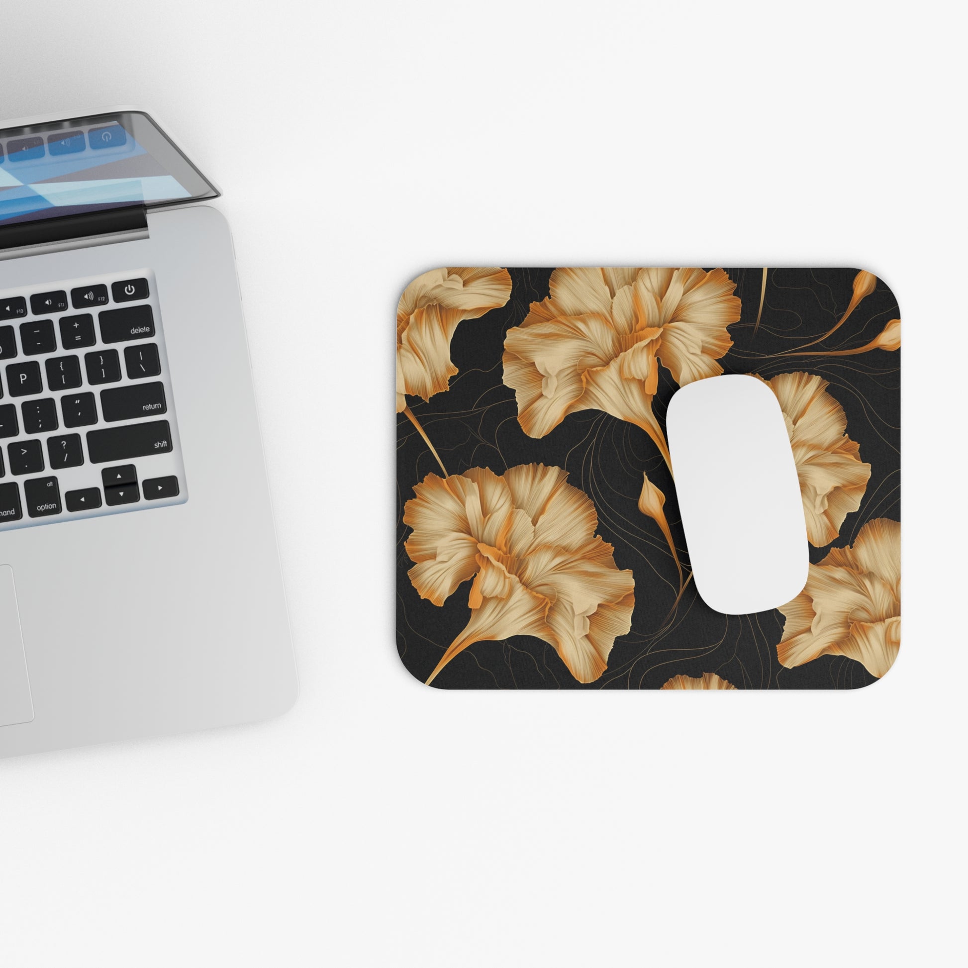 Mousepad with gold floral pattern on black beside an open laptop.