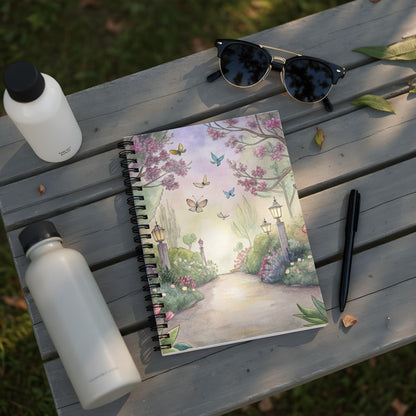 Spiral-bound notebook with watercolor illustration of a garden path with butterflies and cherry blossoms.