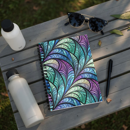 Spiral notebook with stained glass feather pattern on a wooden table.