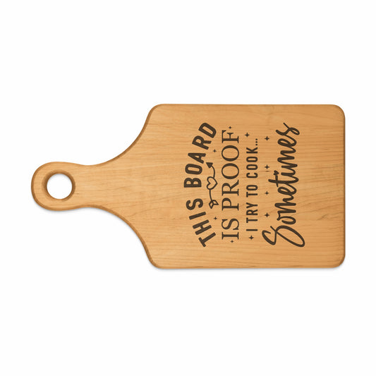 Wooden cutting board with engraved text "This board is proof I try to cook... Sometimes".