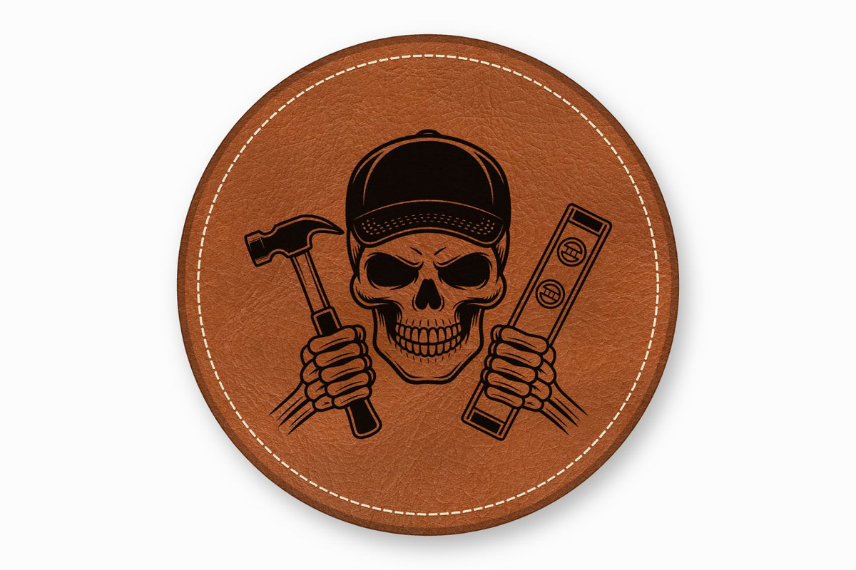 A round brown leather patch with white stitching features a skull wearing a cap, holding a hammer and level.