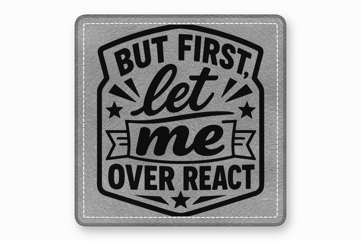 A square gray leather patch featuring black text that reads, "BUT FIRST, let me OVER REACT".