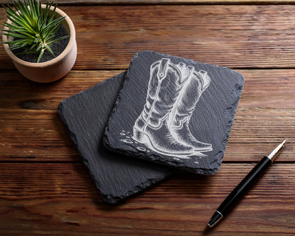 Slate coasters with etched cowboy boots and a pen on a wooden surface.