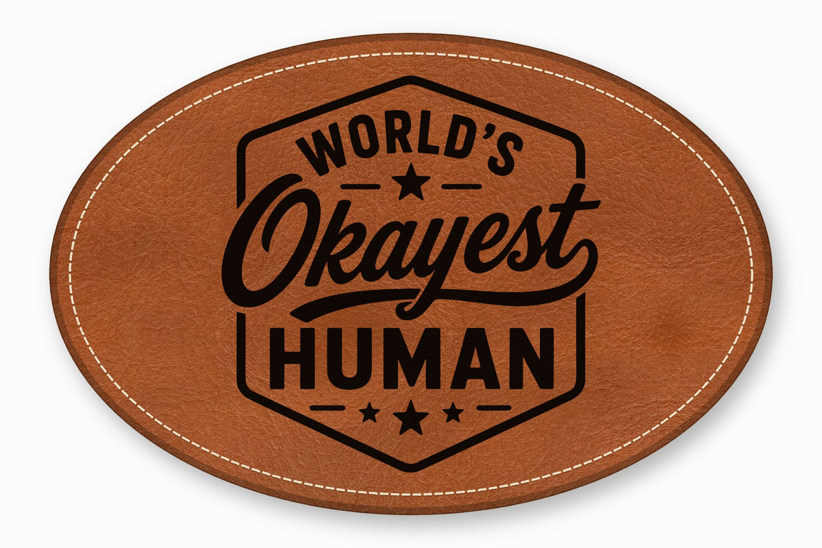 An oval brown leather patch with white stitched edges and black text reading World's Okayest Human.