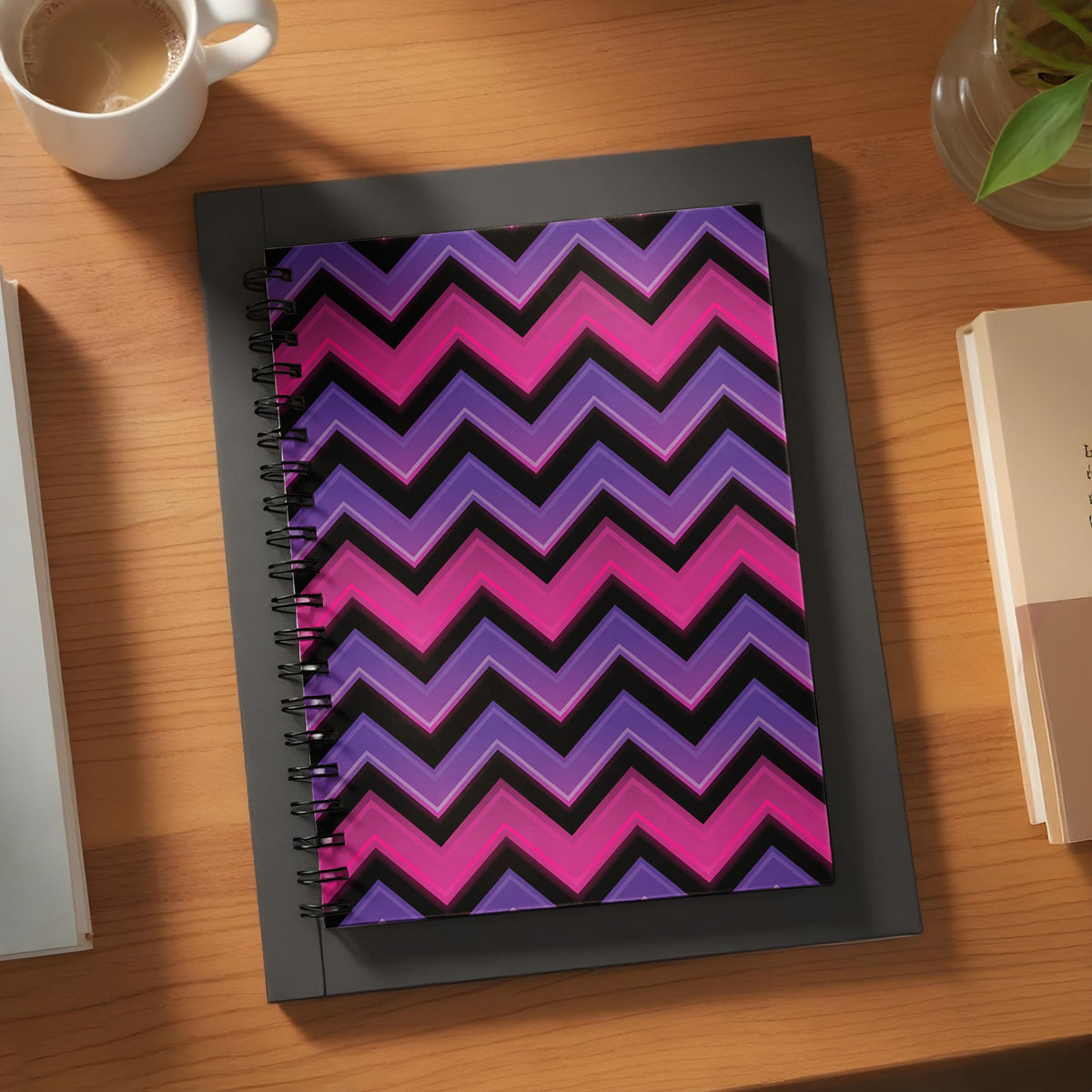 Spiral notebook with a purple, pink, and black chevron pattern on a wooden desk.