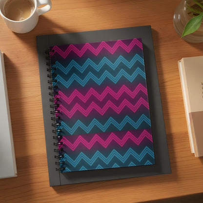 Spiral-bound notebook with pink and blue neon zigzag pattern on dark background.