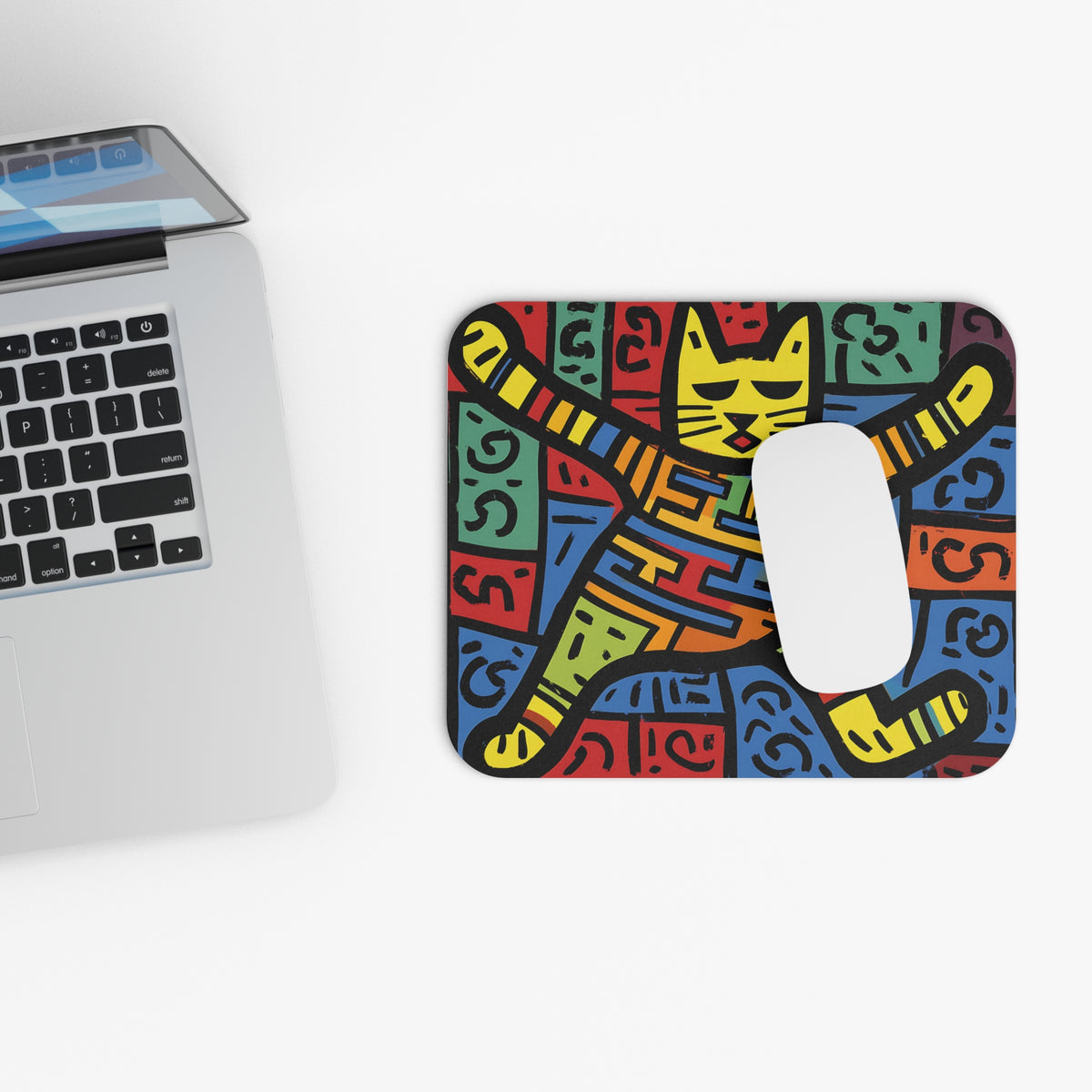 Mousepad with colorful abstract cat design next to a laptop.