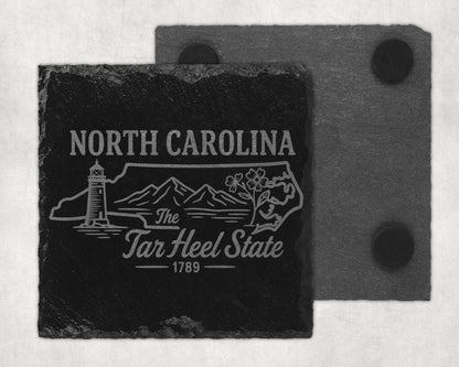 Black slate coaster with North Carolina design, lighthouse, mountains, and flowers.