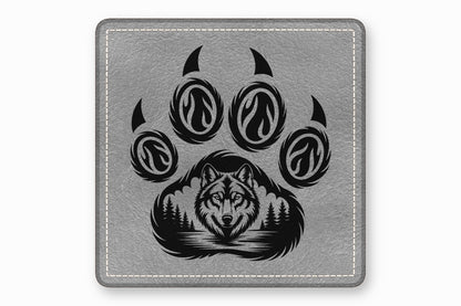 Gray square leather coaster featuring a black engraved paw print containing a wolf and forest design.