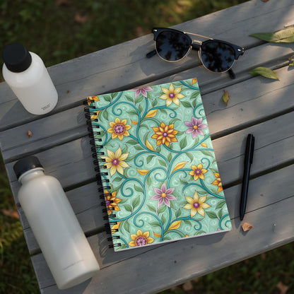 Spiral notebook with floral pattern on a wooden table with water bottles and sunglasses.