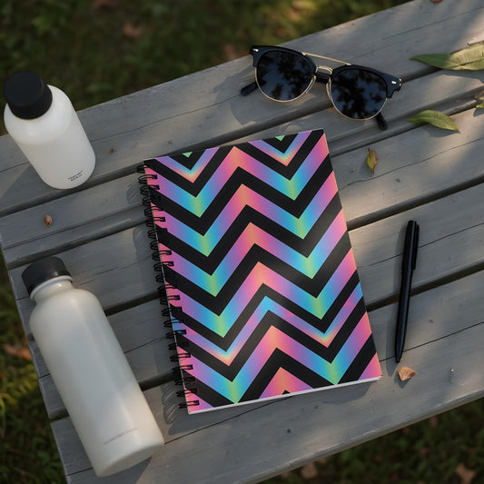 Spiral notebook with black, rainbow chevron pattern on a wooden surface with water bottles.