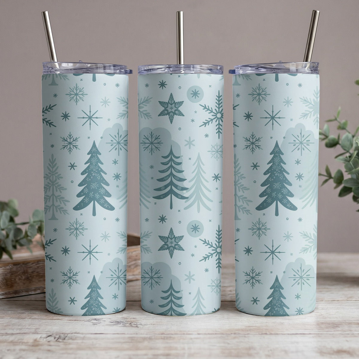 Three tumblers with a blue Christmas tree and snowflake pattern, each with a metal straw.