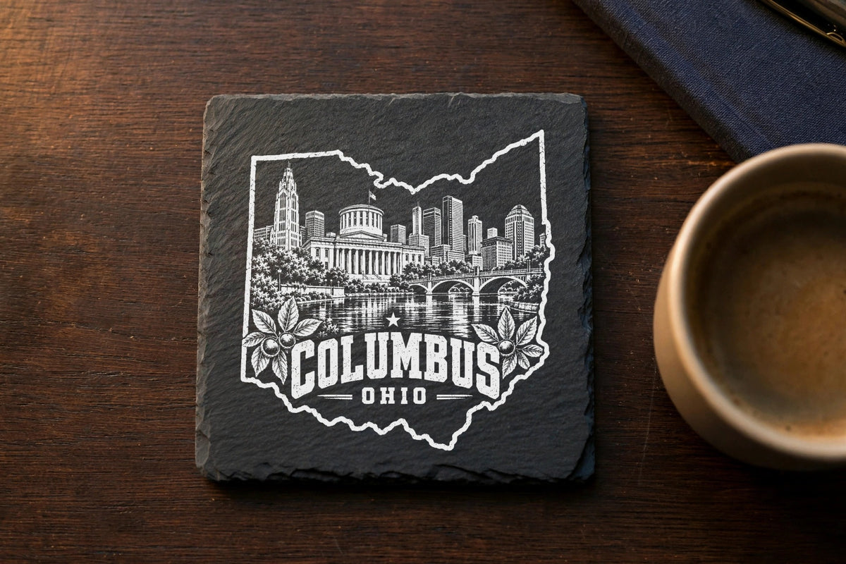 A square black slate coaster engraved with a white design of the Columbus, Ohio skyline inside an outline of the state.