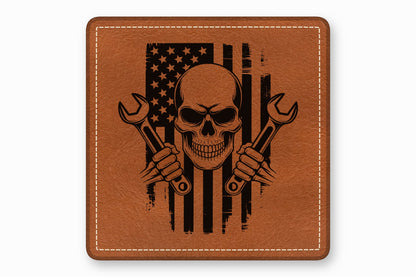 Brown square leather patch with white border stitching and a black distressed American flag, skull, and wrenches design.