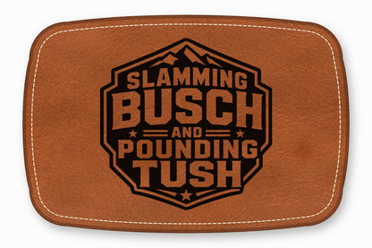 Brown leather patch with white stitching and a black engraved text design that reads Slamming Busch And Pounding Tush.